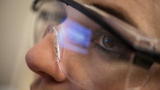 一个研究人员在实验中看着电脑显示器时的脸部特写. 从她的护目镜里可以看到监视器的反射.